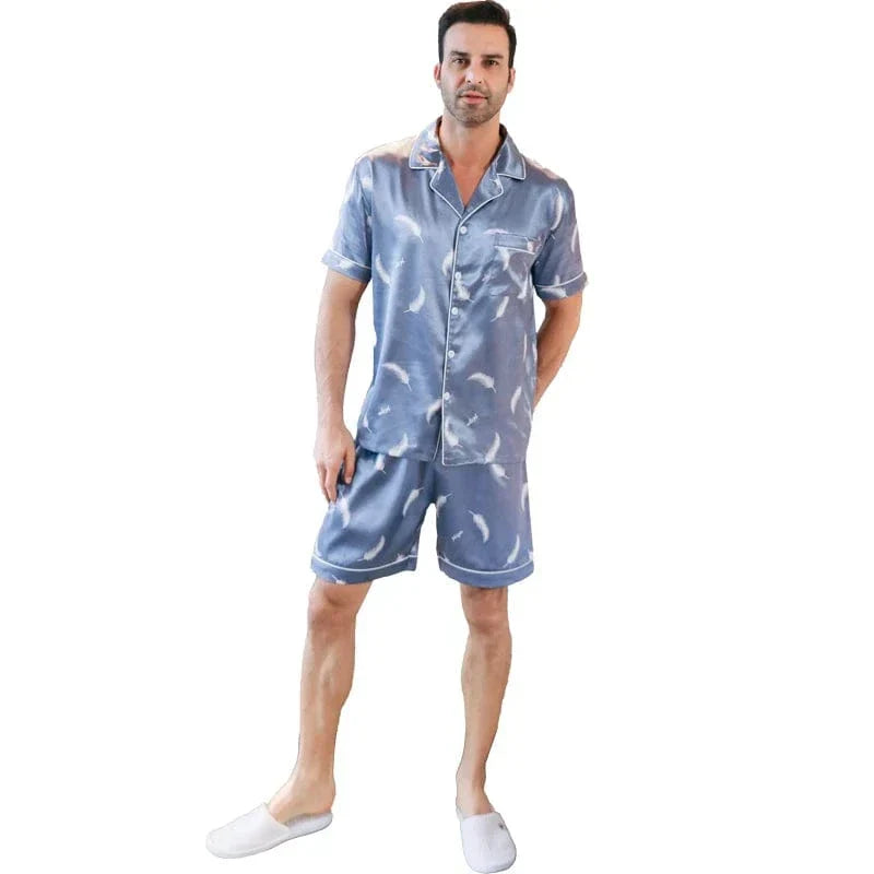 Homme portant le shorty satin Gabriel pour homme, ensemble deux pièces avec chemise boutonnée à manches courtes et short assorti, motif plume clair sur fond bleu, coupe droite, présenté sur fond blanc.