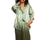 Modèle portant le pyjama femme Garance vert satiné à rayures, chemise ample boutonnée manches longues et pantalon assorti fluide, style doux et confortable sur fond blanc.