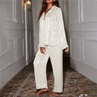 Modèle portant le pyjama femme Garance blanc satiné à rayures discrètes, chemise ample boutonnée manches longues et pantalon fluide assorti, look doux et confortable en intérieur.