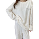 Femme portant un pyjama blanc à manches longues en tissu côtelé doux, composé d’un haut ample et d’un pantalon assorti. Ensemble confortable et élégant, parfait pour les soirées cocooning ou les journées de détente à la maison.