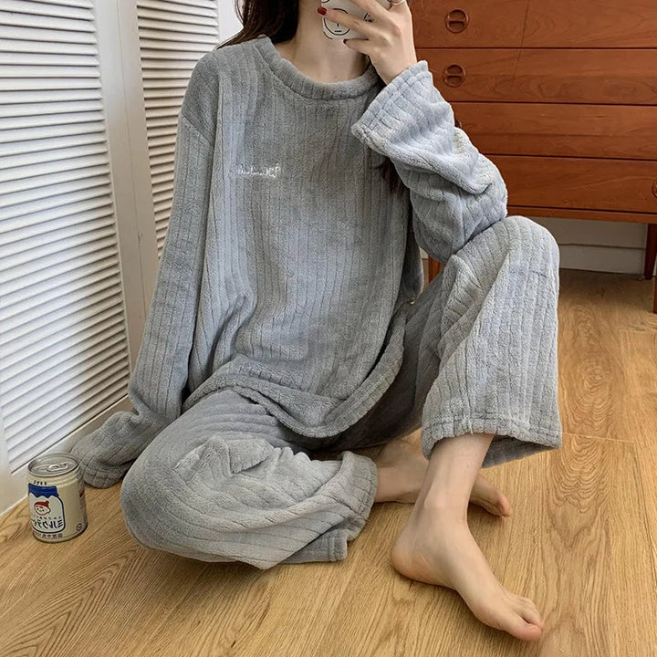 Femme assise portant un pyjama gris en tissu côtelé, composé d’un haut ample à manches longues et d’un pantalon assorti. Ensemble doux, confortable et cosy, parfait pour se détendre à la maison en toute tranquillité.
