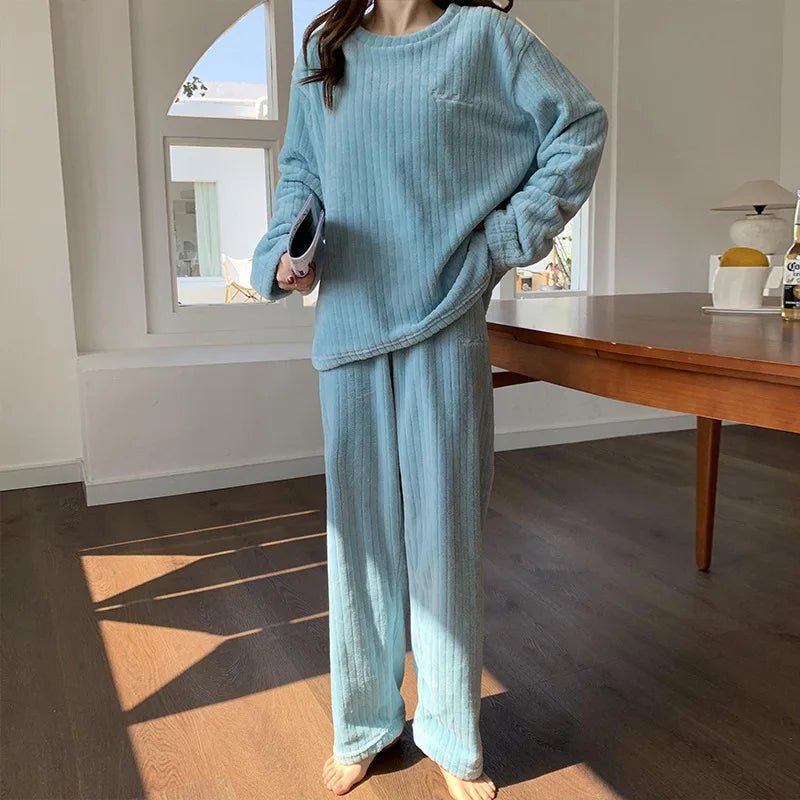 Femme debout portant un pyjama bleu clair en tissu côtelé, composé d’un haut à manches longues et d’un pantalon large assorti. Ensemble doux, confortable et idéal pour se détendre à la maison avec style.
