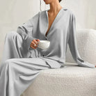 Femme portant le pyjama en coloris gris clair, un ensemble raffiné avec chemise fluide à col ouvert et pantalon ample. Tenue douce, élégante et confortable, idéale pour la nuit et les moments de détente.