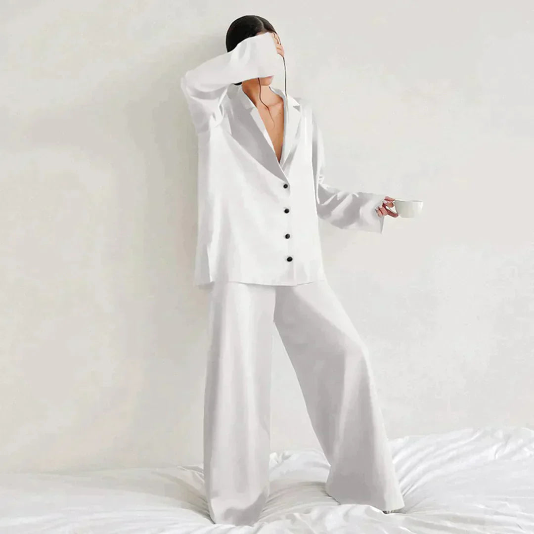 Femme portant le pyjama en coloris blanc, un ensemble chic composé d’une chemise fluide à boutons noirs et d’un pantalon ample. Pyjama doux, élégant et confortable, idéal pour la nuit et les moments de détente.