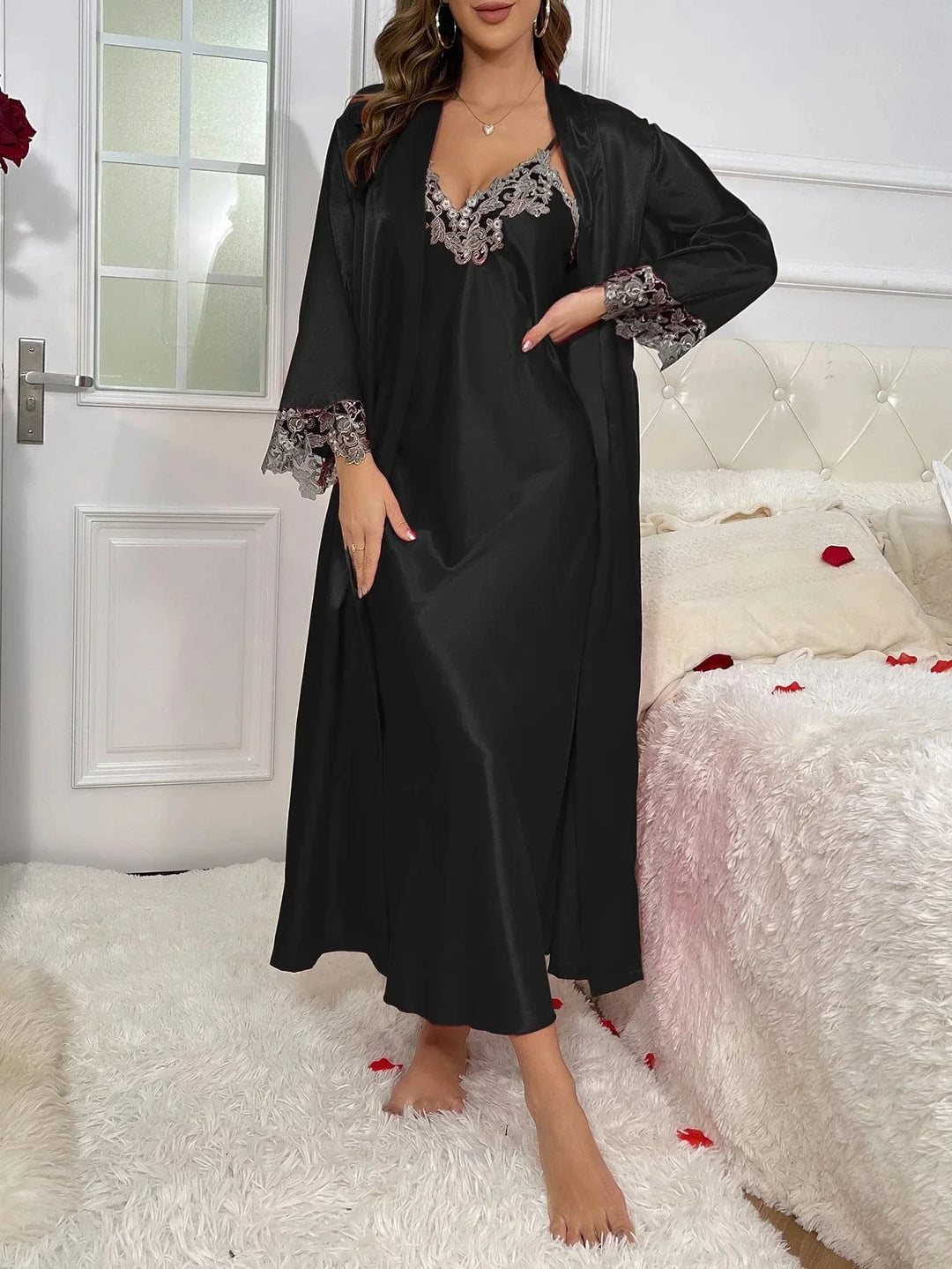 Femme portant l’ensemble Héloïse en satin noir, composé d’une nuisette longue à fines bretelles avec broderies florales au décolleté, et d’un peignoir assorti à manches longues décorées de dentelle. Tenue de nuit élégante, agréable à porter, idéale pour une allure raffinée à la maison.