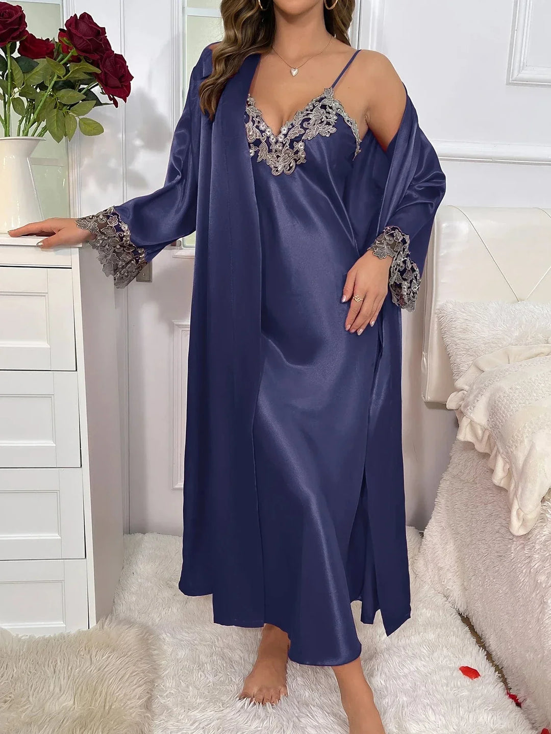 Femme portant l’ensemble Héloïse en satin bleu nuit, composé d’une nuisette longue à fines bretelles avec broderies florales grises au décolleté, et d’un peignoir assorti avec manches longues en dentelle. Lingerie élégante, fluide et agréable, idéale pour des soirées raffinées à la maison.