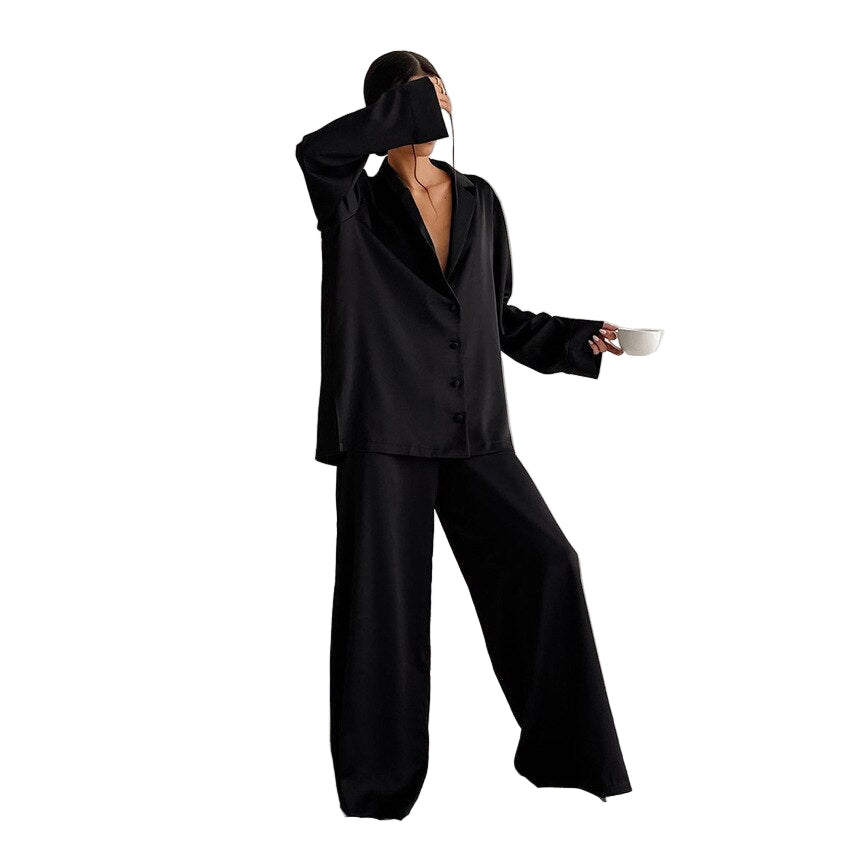 Femme tenant une tasse et vêtue d’un pyjama noir fluide, composé d’une chemise boutonnée à manches longues et d’un pantalon ample. Ensemble léger, élégant et minimaliste, idéal pour les soirées relax ou les matins stylés à la maison.