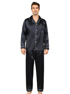Pyjama en satin pour homme de couleur noire, composé d'une chemise à manches longues avec une poche et d'un pantalon assorti. Le pyjama présente des finitions élégantes avec des bordures blanches, ajoutant une touche de sophistication. Le modèle porte ce pyjama avec confort et style, parfait pour se détendre à la maison dans un cadre moderne et raffiné.