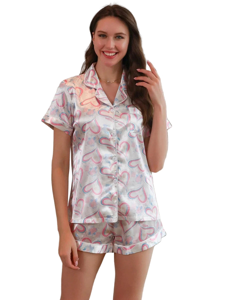 Femme portant le short de pyjama, un ensemble léger et confortable en satin blanc imprimé de cœurs roses et bleus, composé d’une chemise à manches courtes et d’un short assorti, photographiée dans un intérieur lumineux.