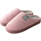 Chaussons unisexe Inaya rose poudré, style matelassé avec étiquette grise, intérieur doublé en tissu doux et chaud, semelle épaisse pour un confort optimal à la maison.