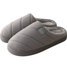 Chaussons unisexe Inaya gris, avec un design matelassé et une étiquette grise. Doublure douce en fourrure et semelle épaisse pour un confort optimal à la maison.