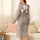 Peignoir femme chaud Iris en tissu peluche gris, coupe mi-longue avec ceinture, capuche avec motif animal et oreilles, porté de dos dans un salon.
