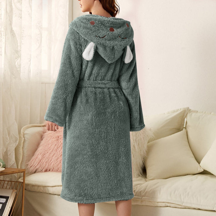 Peignoir femme chaud Iris en tissu peluche vert sauge, coupe mi-longue avec ceinture, capuche fantaisie avec petites oreilles, porté de dos dans un salon.