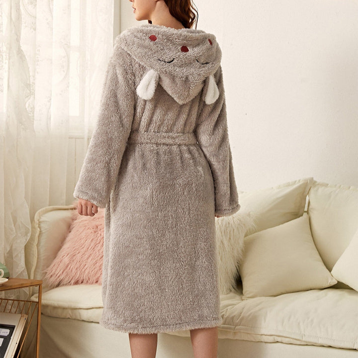 Peignoir femme chaud Iris en tissu peluche gris clair, coupe mi-longue avec ceinture, capuche fantaisie avec petites oreilles, porté de dos dans un salon.
