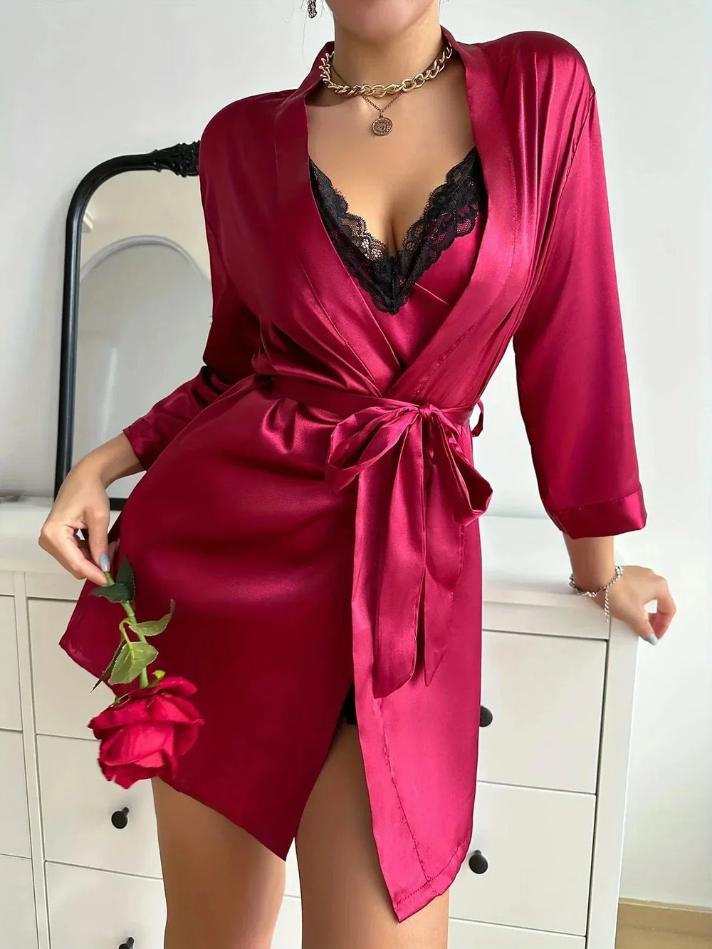 en satin rouge, ceinturé à la taille, laissant apparaître une nuisette assortie ornée de dentelle noire. Le tissu soyeux et la coupe raffinée évoquent élégance et sensualité pour la nuit.