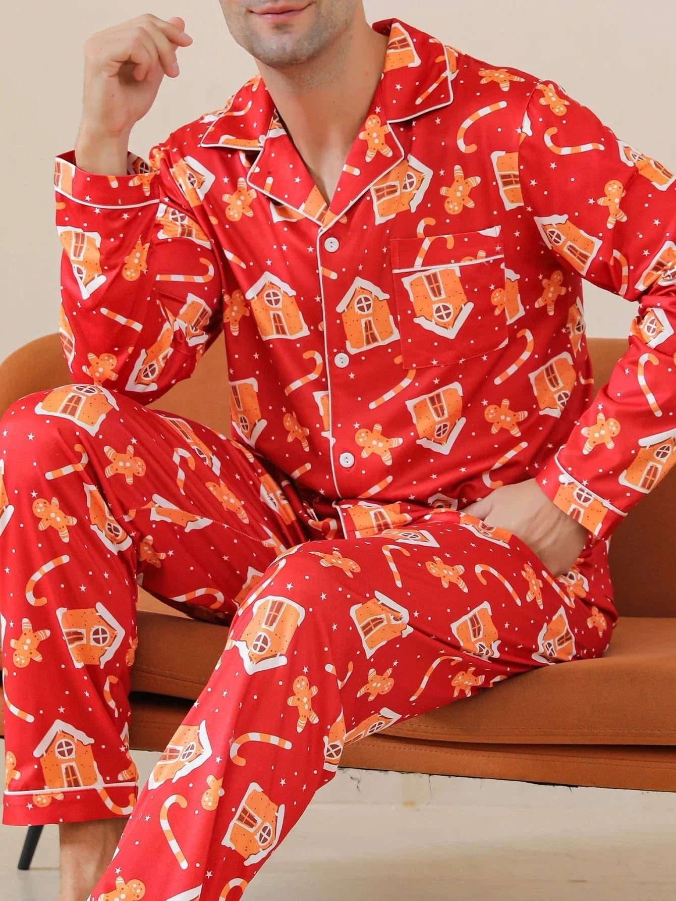 Homme assis portant le pyjama de Noël Jacques pour homme, ensemble deux pièces avec chemise boutonnée à manches longues et pantalon assorti, imprimé festif rouge avec motifs de Noël, vue rapprochée sur le haut et le bas, présenté en intérieur.