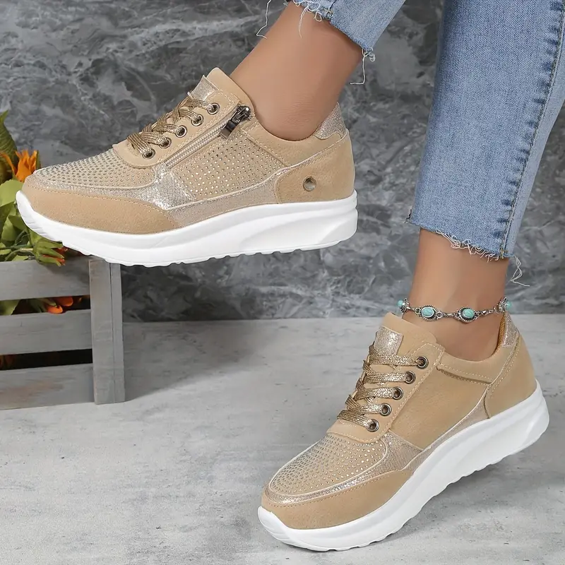 Baskets femme en beige avec des détails métalliques dorés et une finition en cuir suédé. Design moderne et perforé, avec une fermeture éclair latérale et des lacets pour un ajustement parfait. Ces baskets sont idéales pour un look à la fois élégant et confortable, avec une semelle blanche qui offre une excellente adhérence et un confort toute la journée.