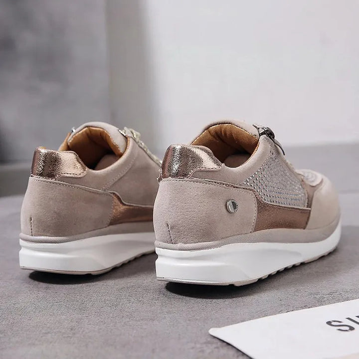 Vue arrière des baskets femme en cuir suédé beige avec des détails métalliques dorés. Design moderne avec une finition brillante et une semelle blanche contrastante, offrant à la fois style et confort. Ces baskets sont idéales pour un look élégant et pratique au quotidien.