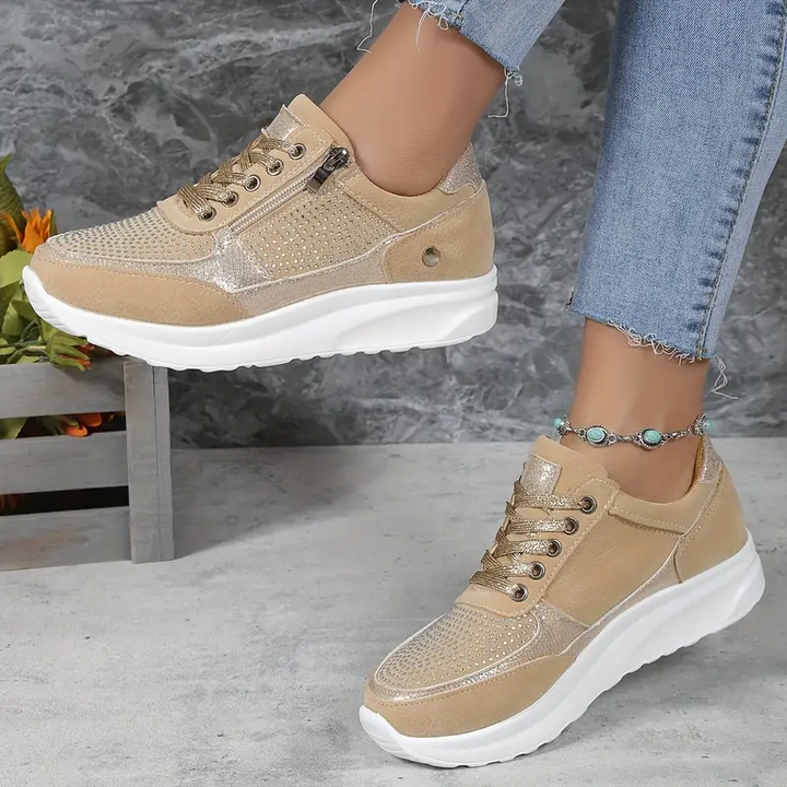 Baskets femme en beige, avec des détails métalliques dorés et une finition en cuir suédé. Design perforé et pratique avec fermeture éclair latérale pour un ajustement facile. Parfaites pour un look décontracté et tendance, elles offrent un confort exceptionnel grâce à leur semelle blanche épaisse et flexible.
