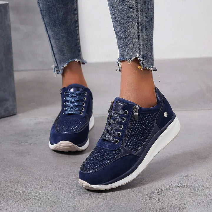 Baskets femme en bleu marine avec des détails métalliques et un cuir suédé élégant. Le design perforé et la fermeture éclair latérale ajoutent une touche moderne, tandis que la semelle blanche épaisse assure confort et soutien. Ces baskets sont parfaites pour un look à la fois tendance et confortable, idéal pour le quotidien.