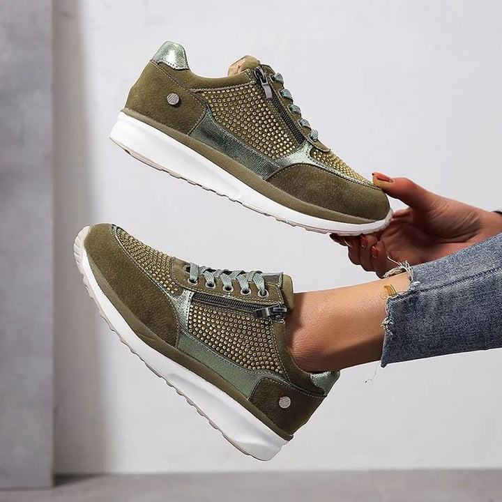 Baskets femme en vert olive avec des détails métalliques argentés et un design perforé élégant. La fermeture éclair latérale et les lacets assurent un ajustement pratique. Ces baskets offrent un style moderne et confortable, avec une semelle blanche épaisse pour un soutien optimal et un confort tout au long de la journée.