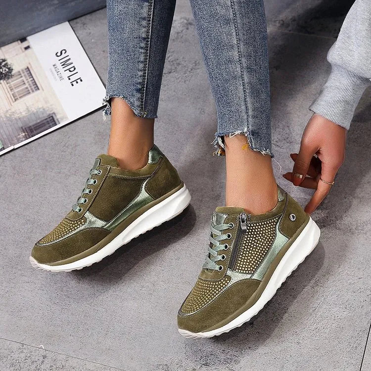 Baskets femme en vert olive avec des détails métalliques argentés et un design perforé. La fermeture éclair latérale et les lacets offrent un ajustement pratique et confortable. Avec une semelle blanche épaisse pour un soutien optimal, ces baskets sont parfaites pour un look moderne et tendance tout en garantissant un confort durable.