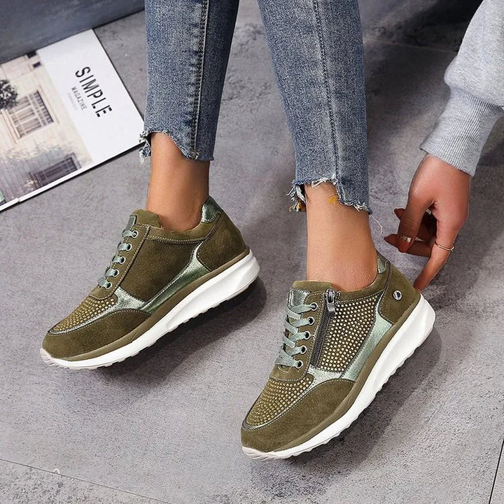 Baskets femme en vert olive avec des détails métalliques argentés et un design perforé. La fermeture éclair latérale et les lacets offrent un ajustement pratique et confortable. Avec une semelle blanche épaisse pour un soutien optimal, ces baskets sont parfaites pour un look moderne et tendance tout en garantissant un confort durable.