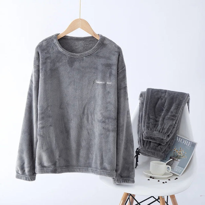 Pyjama en flanelle pour homme composé d’un haut à manches longues gris anthracite suspendu sur cintre et d’un pantalon assorti posé sur une chaise. Ensemble chaud, doux et très confortable, idéal pour l’hiver et les moments cocooning à la maison.
