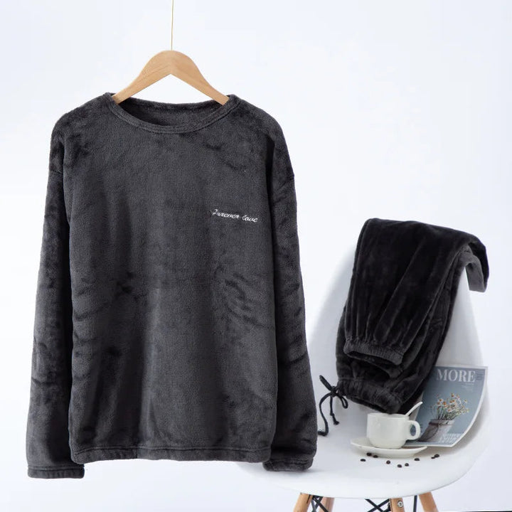Pyjama en flanelle pour homme composé d’un haut à manches longues gris clair suspendu sur cintre et d’un pantalon assorti posé sur une chaise. Ensemble chaud, doux et très confortable, idéal pour l’hiver et les moments de détente à la maison.
