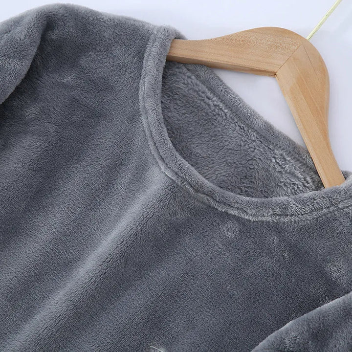 Gros plan sur le haut d’un pyjama en flanelle pour homme, en tissu gris doux et duveteux, suspendu sur un cintre. Matière chaude, moelleuse et très confortable, idéale pour l’hiver.