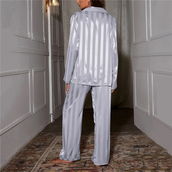 Une femme vue de dos dans un couloir élégant, vêtue d’un pyjama satiné bleu clair à rayures verticales. Les reflets du satin apportent une touche lumineuse et délicate à l’ensemble