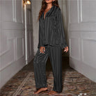 Une femme debout dans un couloir, habillée d’un pyjama satiné noir à rayures verticales. Le contraste de la matière brillante crée une allure chic et raffinée.