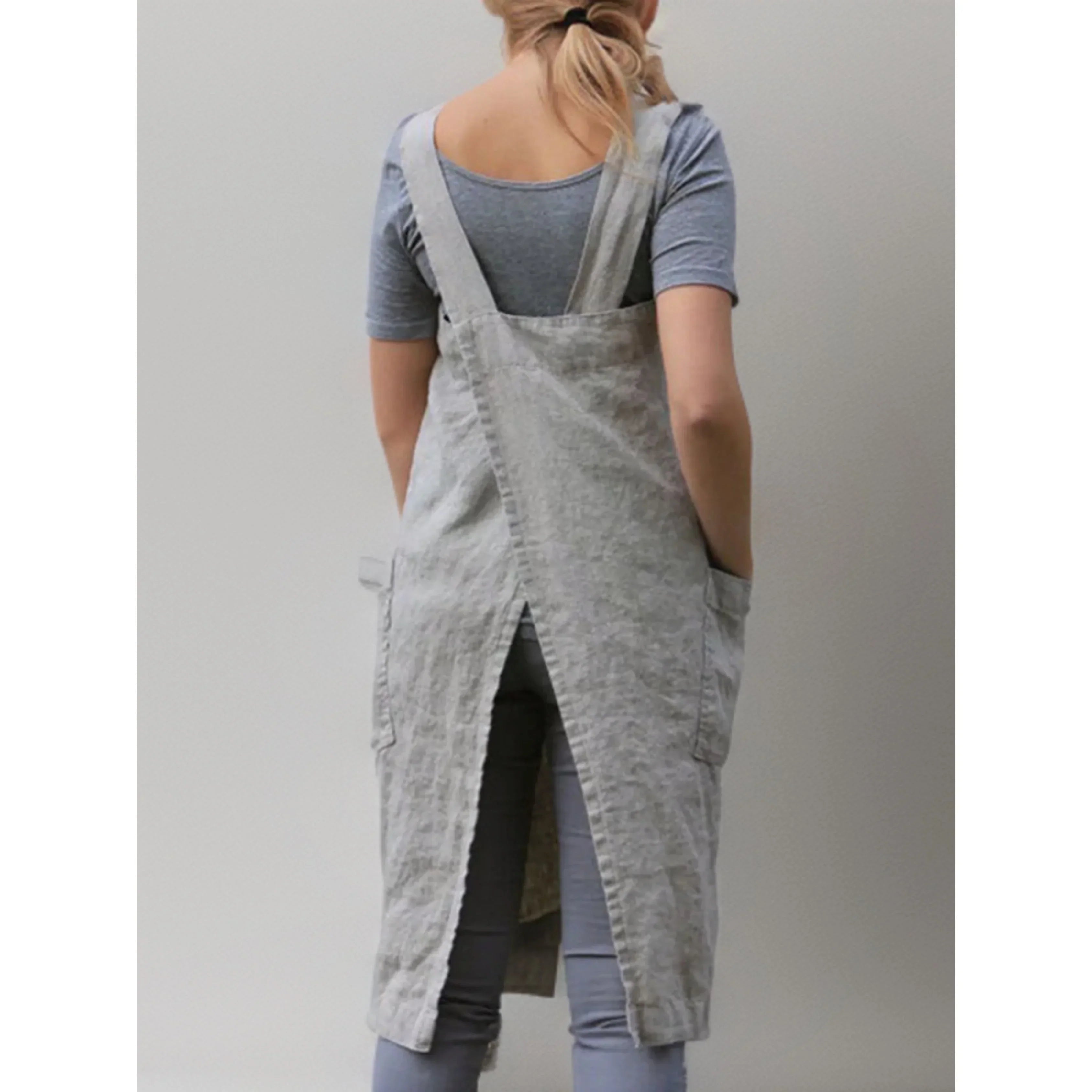Vue arrière du tablier robe femme  pratique et confortable, en lin gris clair, bretelles larges et dos croisé avec fente centrale, porté sur un t-shirt et un legging gris.