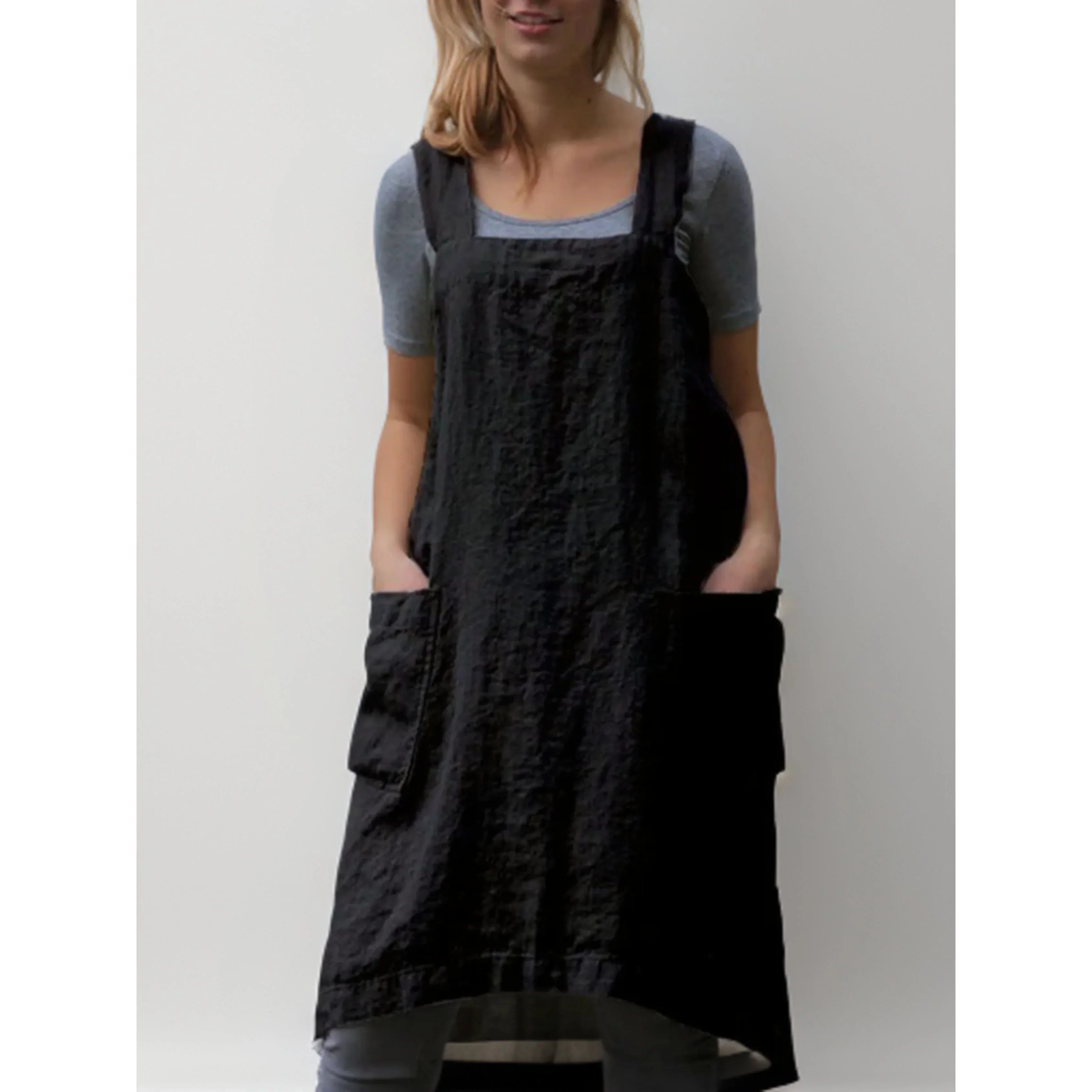 Tablier robe femme pratique et confortable, en lin noir, coupe droite avec larges bretelles et grandes poches avant, porté sur un t-shirt gris.