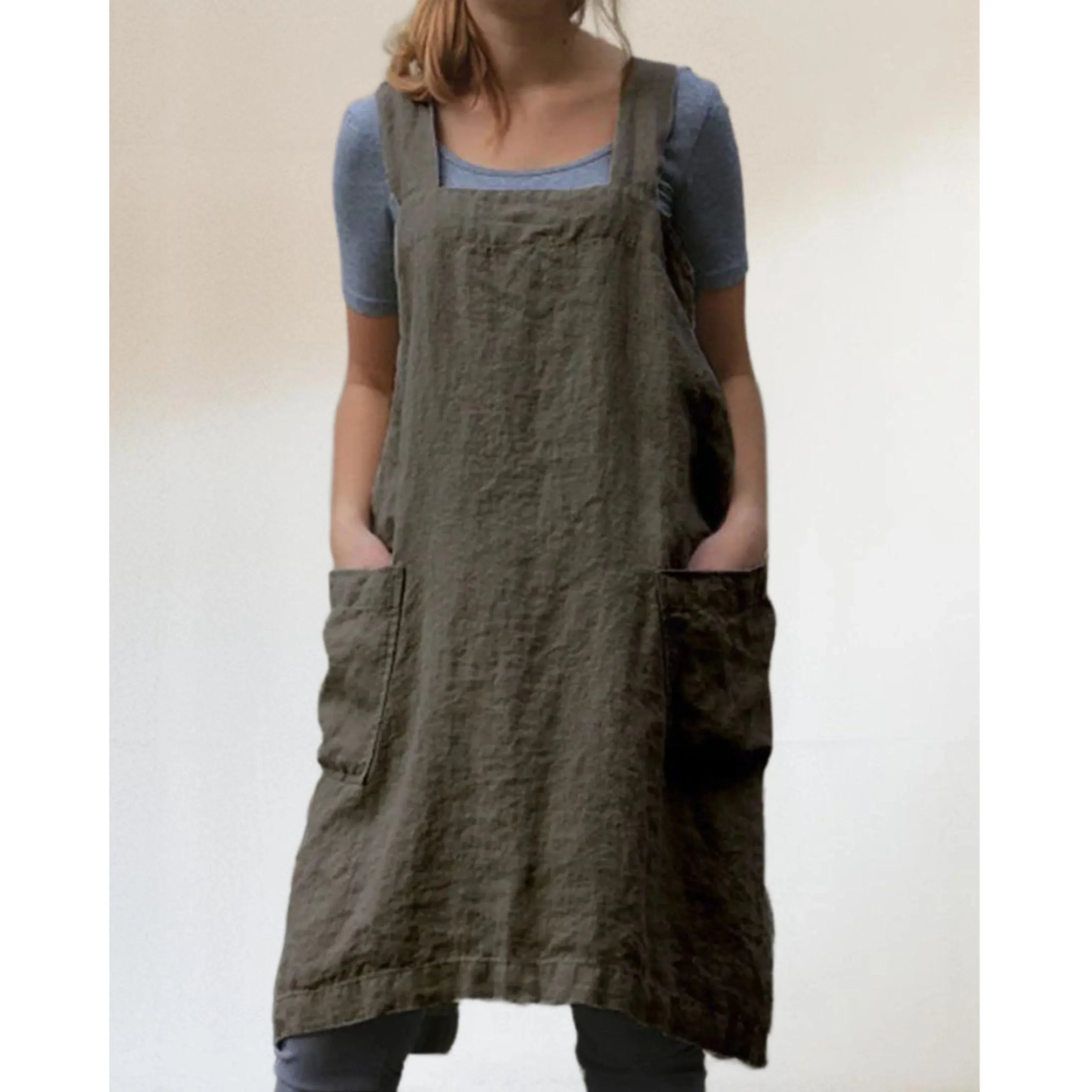 Tablier robe femme pratique et confortable, en lin kaki, coupe droite avec larges bretelles et grandes poches avant, porté sur un haut bleu et un legging gris.