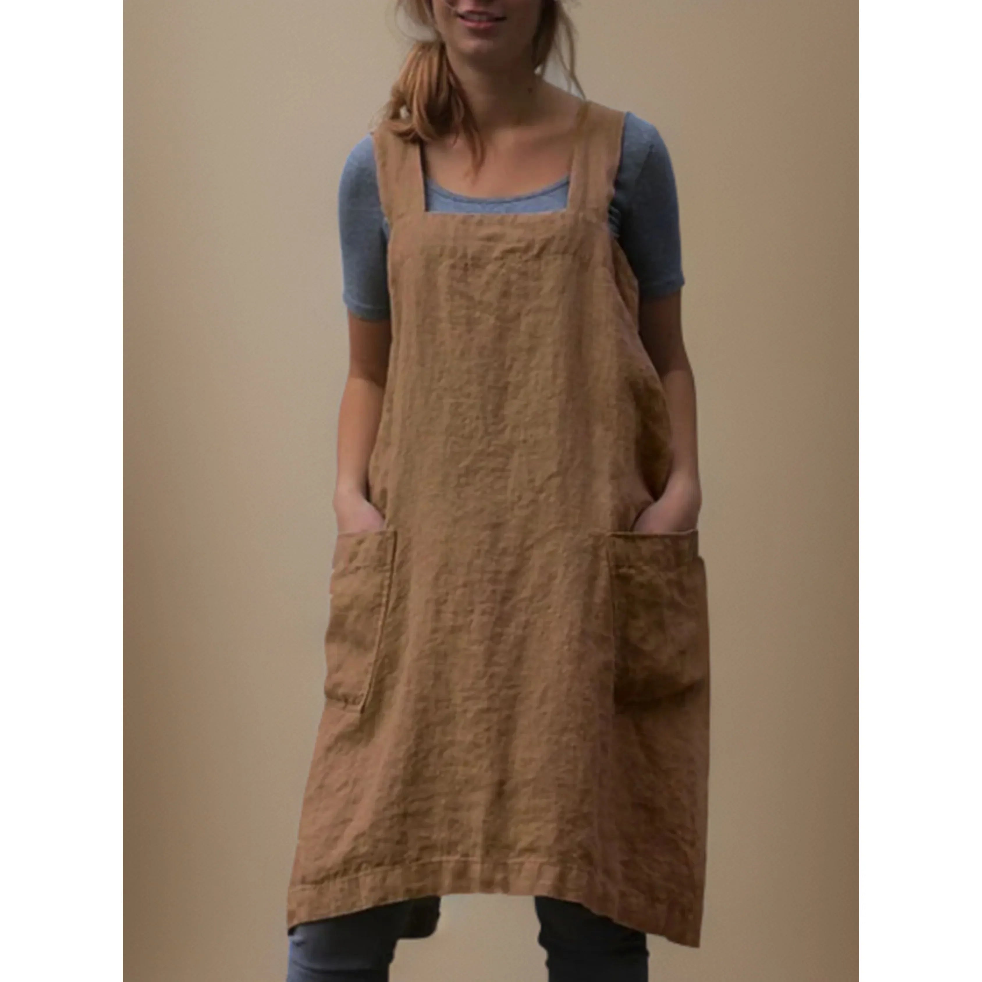 Tablier robe femme pratique et confortable, en lin camel, coupe droite avec larges bretelles et grandes poches avant, porté sur un t-shirt bleu-gris.