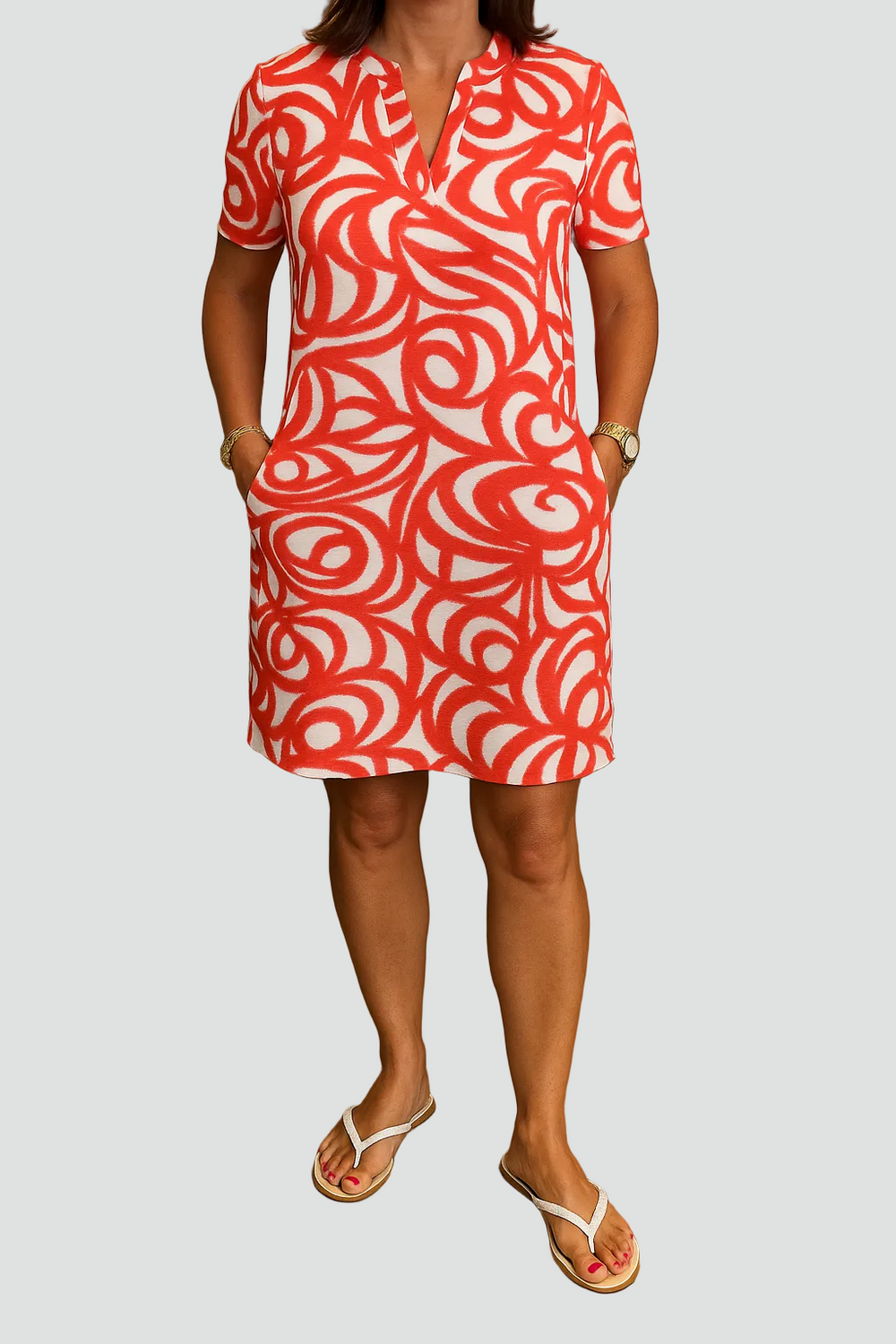 Modèle portant la robe mini Joie avec un imprimé abstrait rouge et blanc. Cette robe légère et tendance, avec des poches pratiques, est parfaite pour l'été. La personne la porte avec des sandales, offrant un look décontracté et stylé, idéal pour les journées ensoleillées.