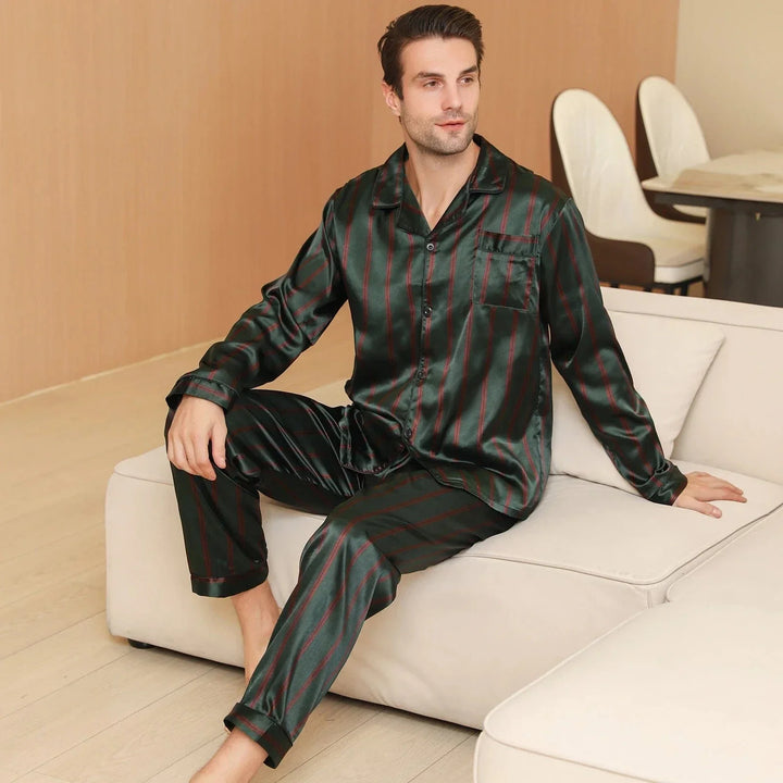 Homme assis sur un canapé portant le pyjama satin pour homme Julien, ensemble léger et agréable composé d’une chemise à manches longues et d’un pantalon assorti, en satin vert à fines rayures rouges, offrant une allure élégante et un confort optimal pour la détente à la maison ou la nuit.