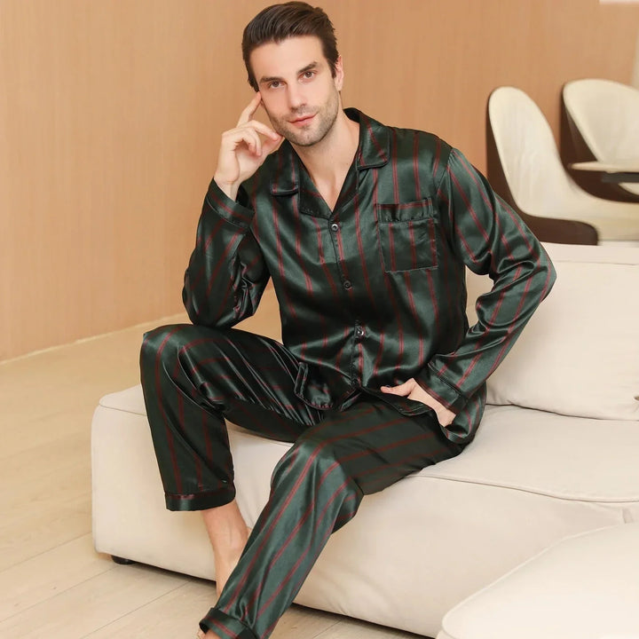 Homme assis sur un canapé portant le pyjama satin pour homme Julien, ensemble léger et agréable en satin vert foncé à fines rayures rouges, composé d’une chemise à manches longues boutonnée et d’un pantalon assorti, offrant une allure élégante et un confort optimal pour la détente à la maison ou la nuit.