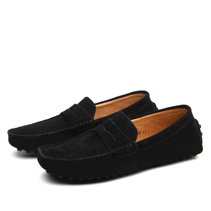 Gros plan sur une paire de mocassins en daim noir pour homme. Les chaussures possèdent une finition soignée avec une texture douce, des coutures visibles et une semelle à picots pour un confort optimal. Parfaites pour un look élégant et décontracté au quotidien.