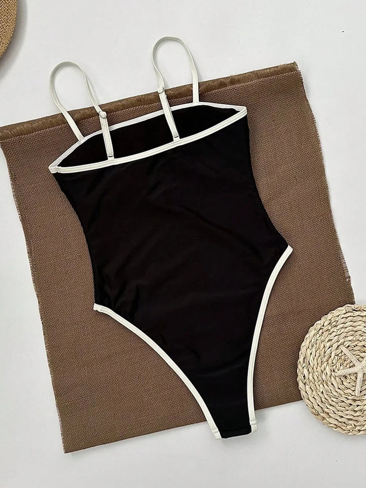 Maillot de bain femme une pièce noir avec bordures blanches contrastées et fines bretelles, présenté à plat sur un tissu texturé, vue arrière pour un style élégant, moderne et confortable.