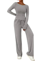 Femme portant un ensemble lounge gris clair composé d’un haut à manches longues ajusté et d’un pantalon large avec cordon à la taille. Tenue douce, fluide et confortable, parfaite pour se détendre à la maison ou pour un look casual chic.