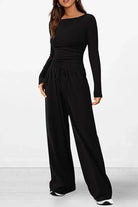 Femme portant un ensemble lounge noir élégant composé d’un haut à manches longues près du corps et d’un pantalon large à taille élastique avec cordon. Tenue douce, confortable et moderne, idéale pour se détendre ou sortir avec style.