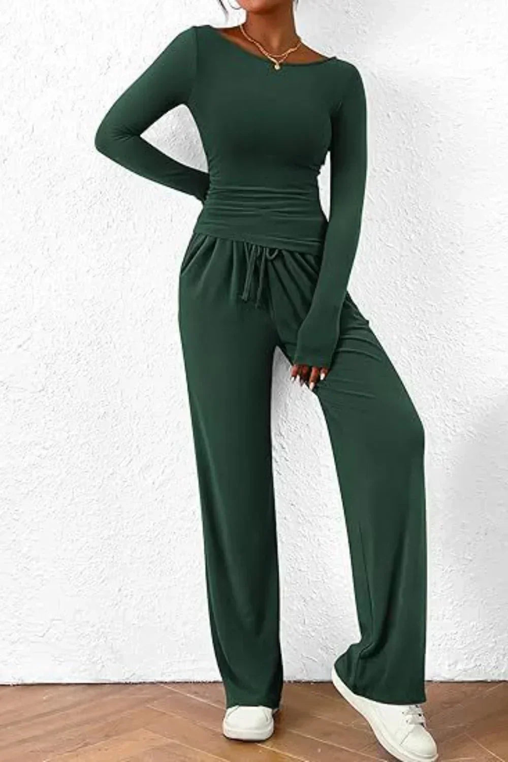 Femme portant un ensemble lounge vert foncé, composé d’un haut à manches longues moulant et d’un pantalon fluide à taille élastique avec cordon. Tenue douce, confortable et élégante, idéale pour le quotidien, les moments de détente ou un style décontracté tendance.