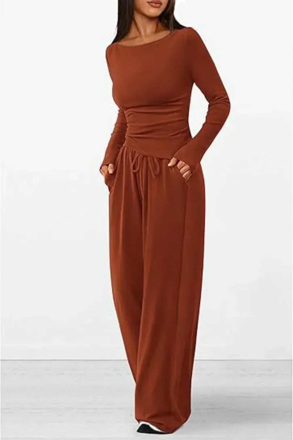 Femme portant un ensemble lounge marron rouille, composé d’un haut à manches longues ajusté et d’un pantalon large avec cordon à la taille et poches latérales. Tenue douce, fluide et confortable, idéale pour les journées détente ou un style casual élégant.