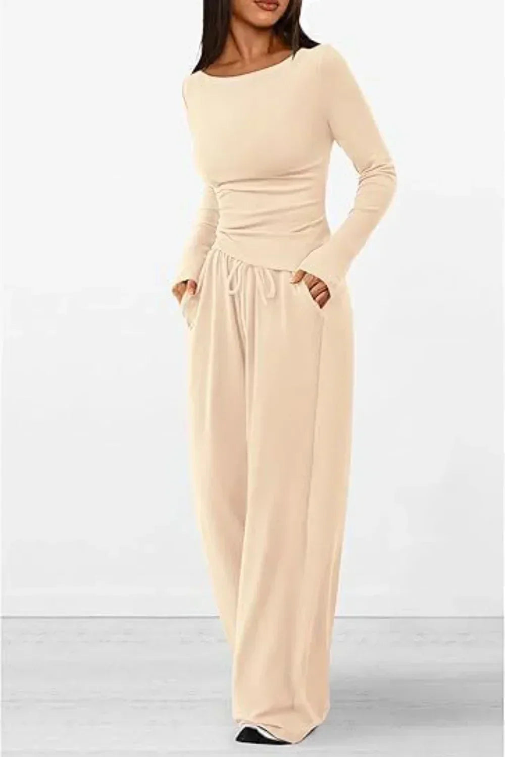 Femme portant un ensemble lounge beige clair, composé d’un haut à manches longues ajusté et d’un pantalon ample avec cordon à la taille et poches latérales. Tenue douce, élégante et confortable, parfaite pour les journées détente ou un look casual raffiné.