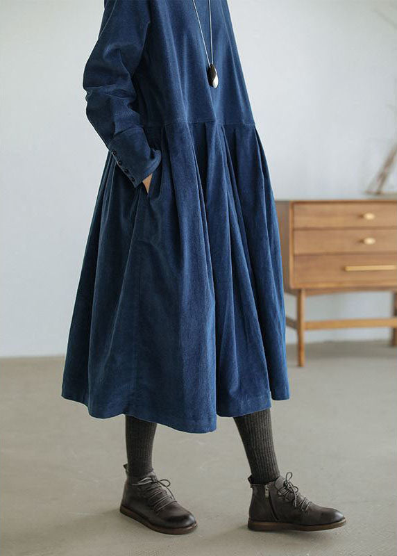 Robe femme élégante et raffinée, bleu marine, coupe ample midi avec jupe plissée et poches, manches longues boutonnées, portée avec collants foncés et bottines en cuir.