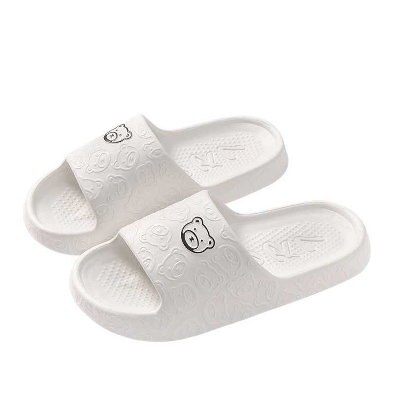 Chaussons femme Kyara blancs, avec un design ludique de petites têtes d'ours sur la bande, offrant confort et style pour se détendre à la maison.