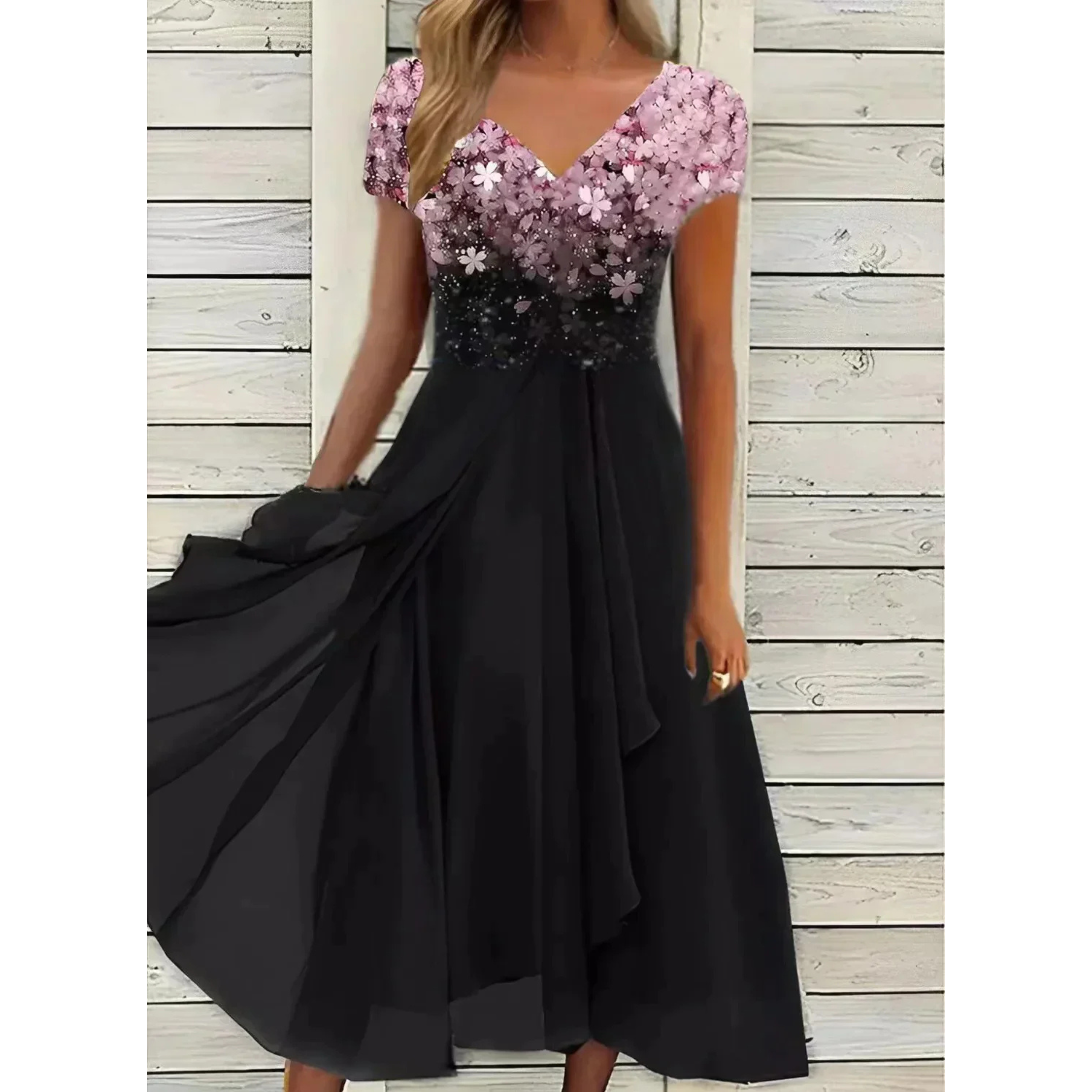 Robe femme élégante et polyvalente, longue et fluide, jupe noire avec haut floral rose/violet dégradé, col en V et manches courtes, portée devant un mur en bois blanc.