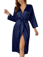 Femme souriante portant le peignoir en satin bleu marine Léa, avec une coupe croisée élégante, ceinture assortie à la taille et manches longues, parfait pour une allure chic et confortable à la maison.